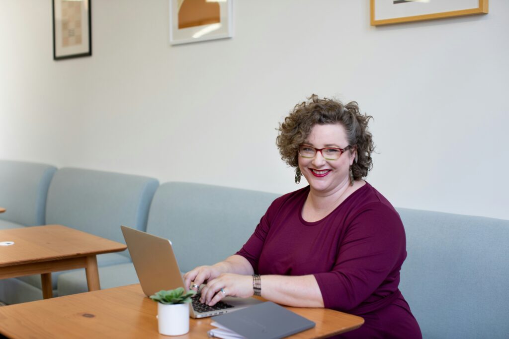 A smiling woman sitting in a cafe in front of her laptop - happy to be getting help from a virtual assistant
